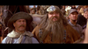 Two men in old western attire stand among a crowd, as if stepping out of Tall Tale (1995) DVD. One wears a wide-brimmed hat and scarf, the other has a fur hat, bushy beard, and beaded clothes. Both look ahead in surprise.