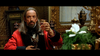 A man with long hair in a red robe holds up a glass of wine at a lavish table, a Sphynx cat on his lap—reminiscent of classic scenes from Tall Tale (1995) DVD, surrounded by ornate gold decor.