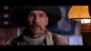 A serious-looking man with a large mustache, wide-brimmed hat, and bandana sits by a warm yellow lamp in a dim room—evoking the classic western spirit of Tall Tale (1995) DVD.