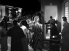 In a scene from the DVD Kiss Her Goodbye (1959), a group of people stands outside a motel room at night, watching as a man enters through the doorway.