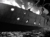 Black-and-white scene from The Cruel Sea (1953) DVD showing a ship engulfed in flames with figures abandoning the vessel into the water.