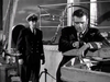 Two naval officers in uniform stand on the deck of a ship in a scene from The Cruel Sea (1953) DVD.