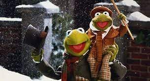 Kermit the Frog, in winter clothes and carrying a smaller frog, appears in a snowy scene from The Muppet Christmas Carol with Michael Caine—now available on The Muppet Christmas Carol DVD (1992).