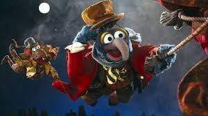 Gonzo, in Victorian attire and a top hat, swings on a rope beneath the moonlit sky—a whimsical scene from The Muppet Christmas Carol DVD (1992) holiday movie, with another similarly dressed Muppet behind him.