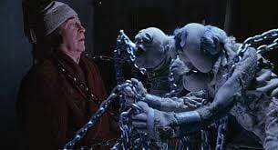 An older man in a nightcap and robe looks worried as two ghostly, chained figures approach him in a dark scene, echoing Michael Caine’s role in The Muppet Christmas Carol DVD (1992).
